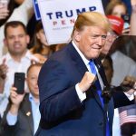 Economic D‑Day: Trump Targets Iran’s Lifelines man in suit raising fists at a rally podium