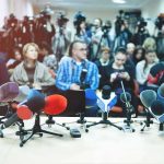Media Giant in Legal Crosshairs Row of microphones on a table at a press conference