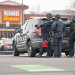 Police officers gather beside a patrol SUV at a taped-off scene