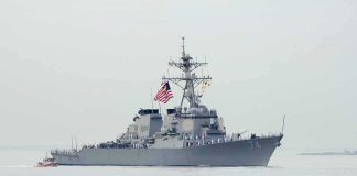Navy destroyer with crew lined on deck at sea
