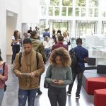 Students walking through a bright campus atrium using mobile devices