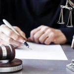 Judge writing at desk with gavel and Lady Justice statue