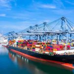 Sneaky New Tax Lands Hard Container ship docked at a busy industrial port.
