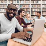 Shock Count: 188 Lines — Files Still Sealed Smiling man using a laptop in a library study group