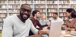 Smiling man using a laptop in a library study group