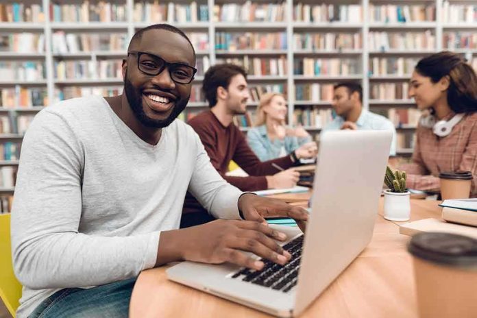 shutterstock_1057976711 Smiling man using a laptop in a library study group