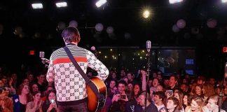 Guitarist performing on stage facing a cheering crowd