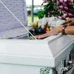 Autopsy Pending After Model’s Death hands resting on a white casket with flowers nearby