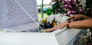hands resting on a white casket with flowers nearby