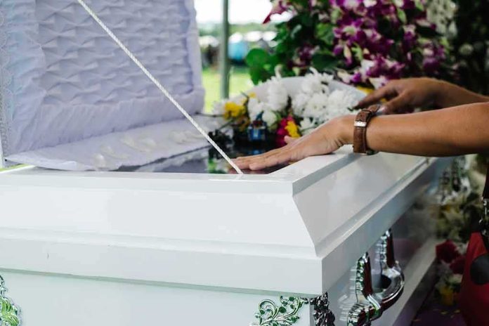 shutterstock_1213485397 hands resting on a white casket with flowers nearby