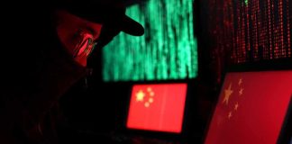 Hooded person using a laptop with Chinese flags on screens