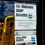 Tax-Funded Groceries, No ID Needed Store window with SNAP benefits signs and yellow shopping carts