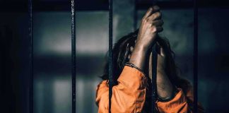 Prisoner in orange jumpsuit gripping jail bars