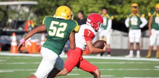 Football player in red runs with the ball as defender in green attempts a tackle