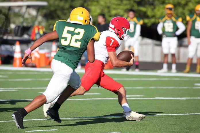 shutterstock_1537816895 Football player in red runs with the ball as defender in green attempts a tackle
