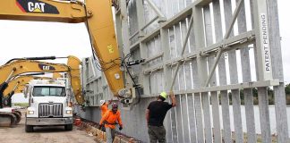 Construction workers install large steel wall panels with excavators