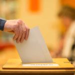Hand placing a ballot into a wooden voting box