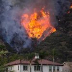 Red Flags, Evacuations—System Cracks Exposed Wildfire burning on a hillside near homes