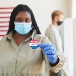 Generational Revolt Meets Brick Wall Voter wearing a mask holds an I Voted sticker at a polling place