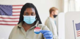 Voter wearing a mask holds an I Voted sticker at a polling place