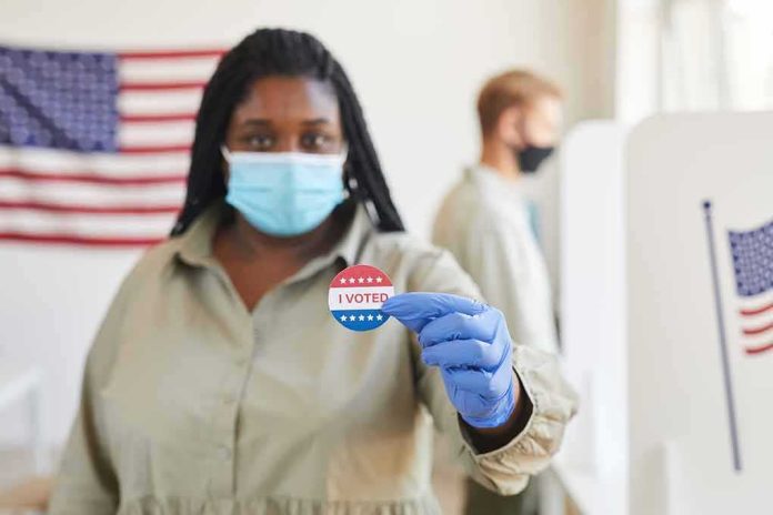 shutterstock_1810359373 Voter wearing a mask holds an I Voted sticker at a polling place