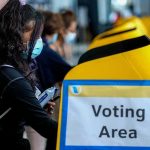 Rigged Scoreboard? Trump’s 99% Win Mirage voter wearing a mask using a yellow ballot box