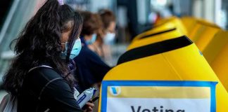voter wearing a mask using a yellow ballot box