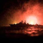 Energy Chokehold: Tankers Torched Near Oman Warship silhouette at sea against fiery glow