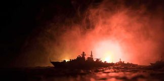Warship silhouette at sea against fiery glow