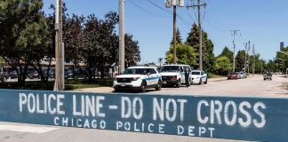 Police line barrier blocking a street with patrol vehicles behind
