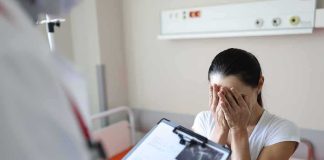 Woman covering her face while doctor holds a clipboard in a hospital room