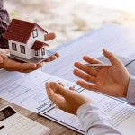 Rental Ad Shakeup—Rivals Forced To Race Hands discussing real estate with a small house model and documents