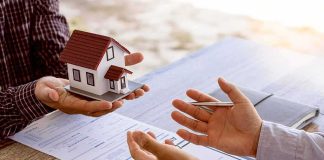 Hands discussing real estate with a small house model and documents