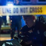 Police officer examines evidence at night behind caution tape
