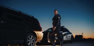 Police officer standing near patrol car during twilight traffic stop