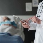 A Temporary Drug Deal With Permanent Questions Doctor using tablet beside hospital patient