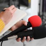 AI Cameras Roll—Evidence Still Missing Journalist holding two microphones while writing in a notebook