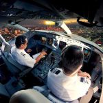 Pilots in an airplane cockpit during city approach at sunset