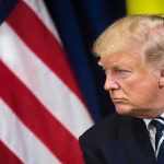 Gold Dollar Frenzy—Guess Who’s On It man in suit with striped tie beside American flag