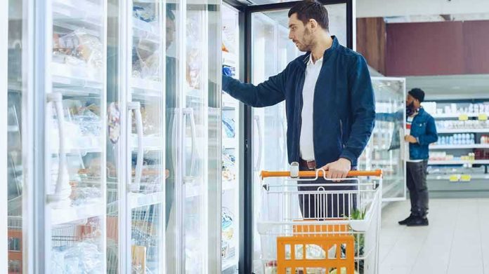 Man with shopping cart opens freezer door in grocery store