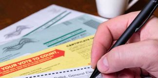 Hand filling out a mail-in ballot with a pen