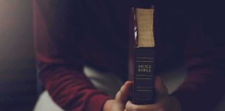 Gospel Bombshell: Lazarus Sparks Deadly Plot Person holding a closed Bible while seated