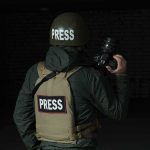Press photographer in helmet and vest holding a camera