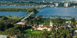 Aerial view of a waterfront estate with pool, lawns, and palm trees